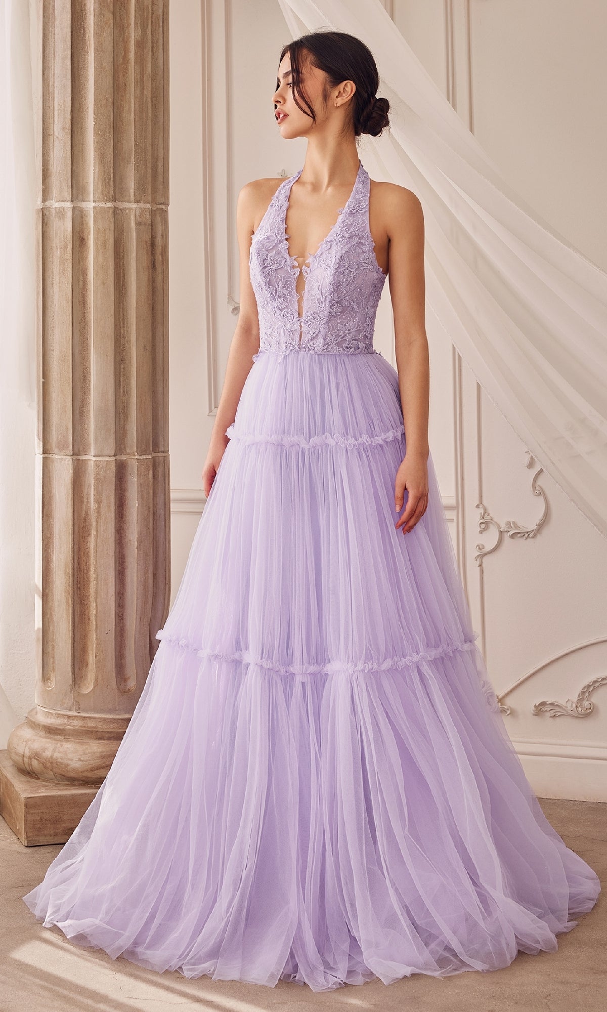 A woman stands indoors wearing the Lace-Halter Long A-Line Prom Dress A1206, an elegant floor-length lavender gown with a floral-lace bodice and layered tulle skirt.